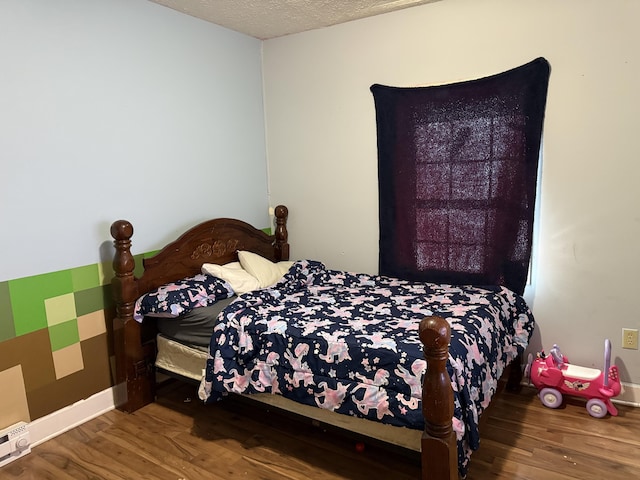 bedroom featuring a textured ceiling, a baseboard heating unit, baseboards, and wood finished floors