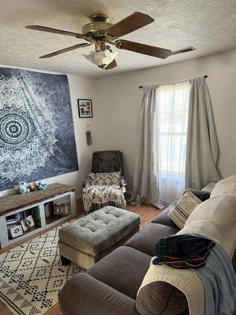 living room featuring ceiling fan, wood finished floors, and a textured ceiling