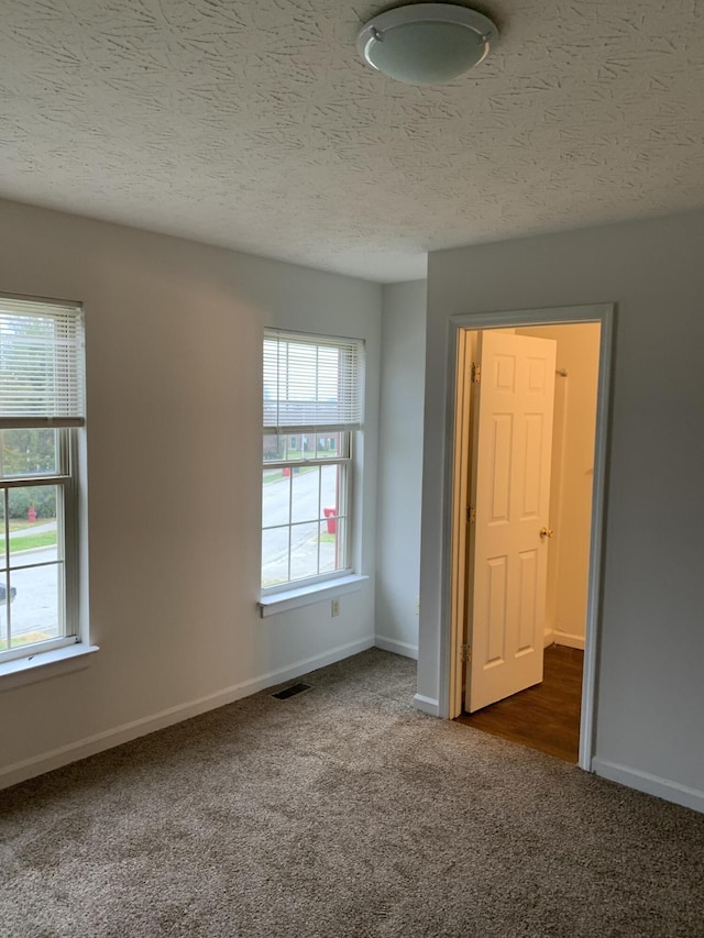 empty room with a textured ceiling, visible vents, dark colored carpet, and baseboards