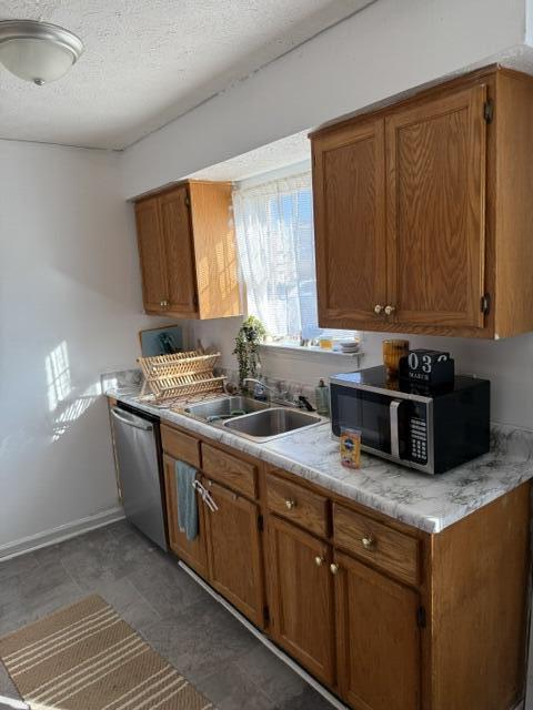 kitchen with brown cabinetry, a sink, light countertops, appliances with stainless steel finishes, and a textured ceiling