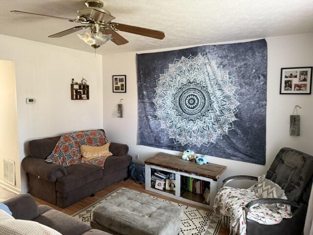 living room featuring ceiling fan, wood finished floors, visible vents, and a textured ceiling