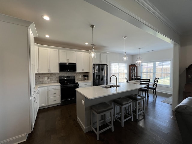 kitchen with tasteful backsplash, light countertops, a kitchen breakfast bar, black appliances, and a sink