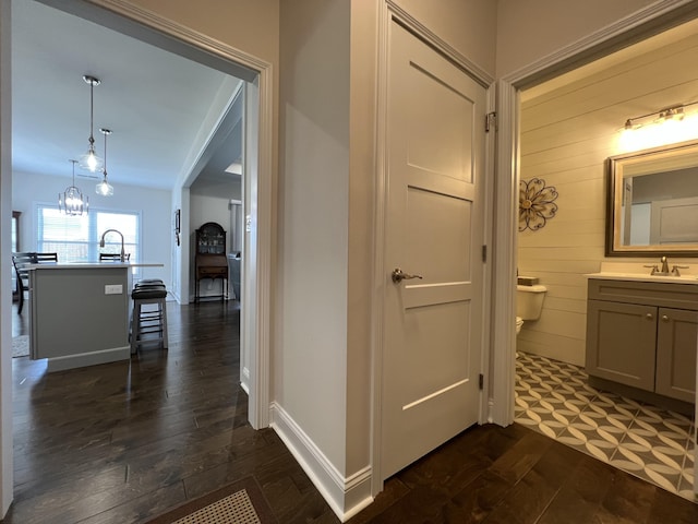 hall featuring a notable chandelier, a sink, baseboards, and dark wood-style flooring