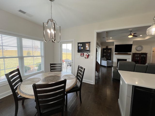 dining room with visible vents, ceiling fan with notable chandelier, dark wood finished floors, a fireplace, and baseboards