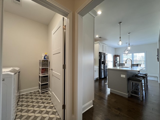 kitchen with baseboards, white cabinets, a kitchen bar, refrigerator with ice dispenser, and independent washer and dryer