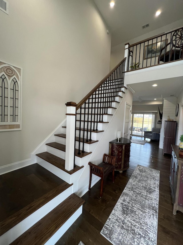 staircase with wood finished floors, visible vents, a towering ceiling, and baseboards