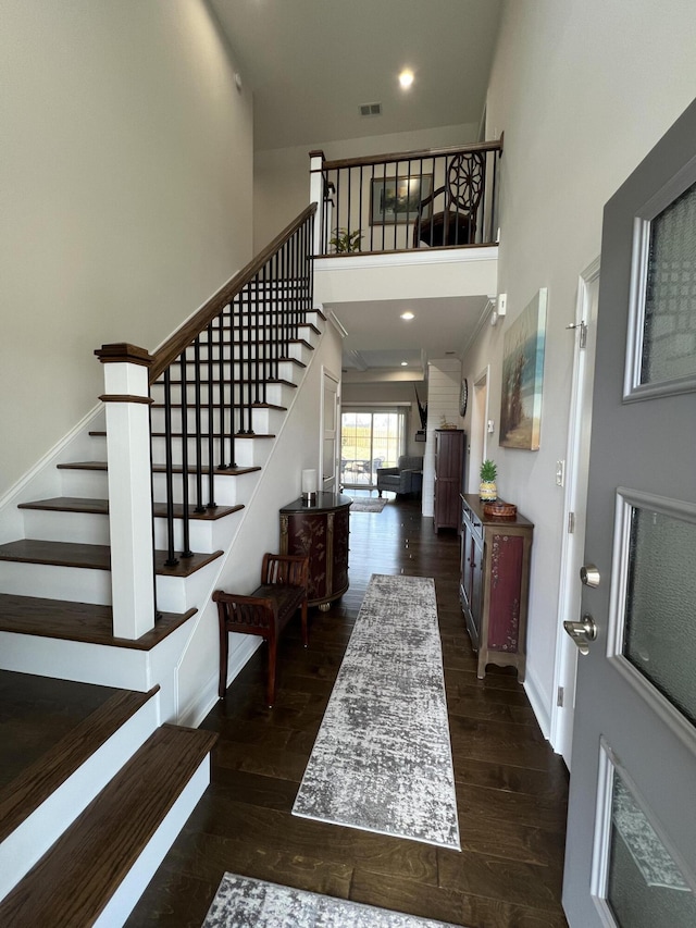 foyer entrance featuring visible vents, wood finished floors, a towering ceiling, and stairway