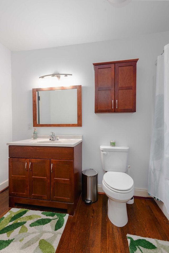 bathroom with vanity, toilet, wood finished floors, and baseboards