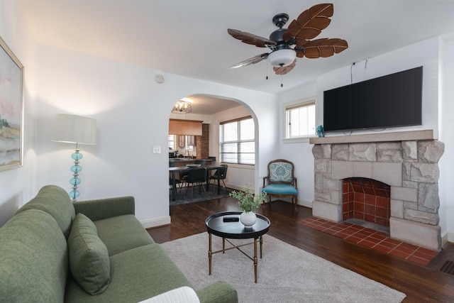 living room with wood finished floors, arched walkways, a fireplace, baseboards, and ceiling fan