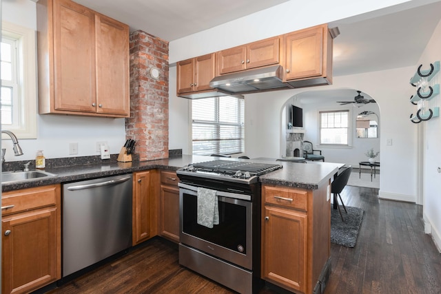 kitchen with a peninsula, arched walkways, a sink, under cabinet range hood, and appliances with stainless steel finishes