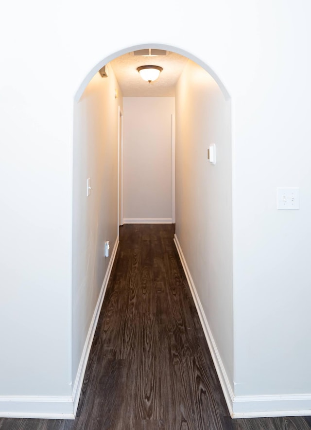 hallway featuring wood finished floors, baseboards, and arched walkways