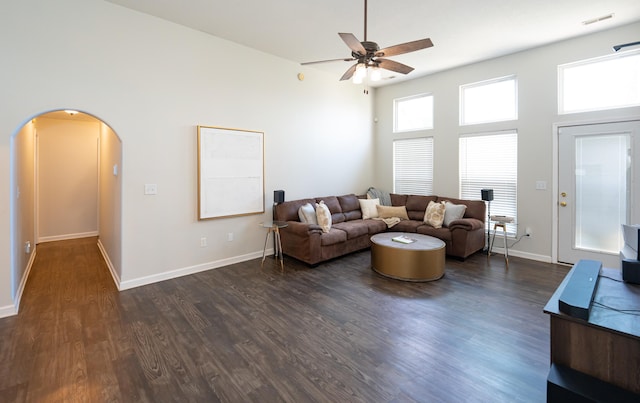 living room featuring visible vents, a ceiling fan, dark wood-style floors, arched walkways, and a high ceiling