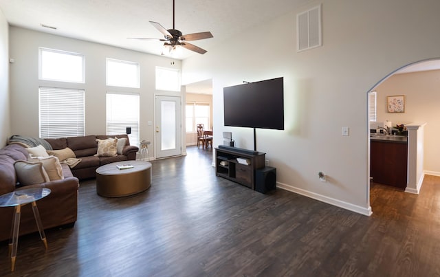 living room featuring dark wood finished floors, a ceiling fan, visible vents, and arched walkways