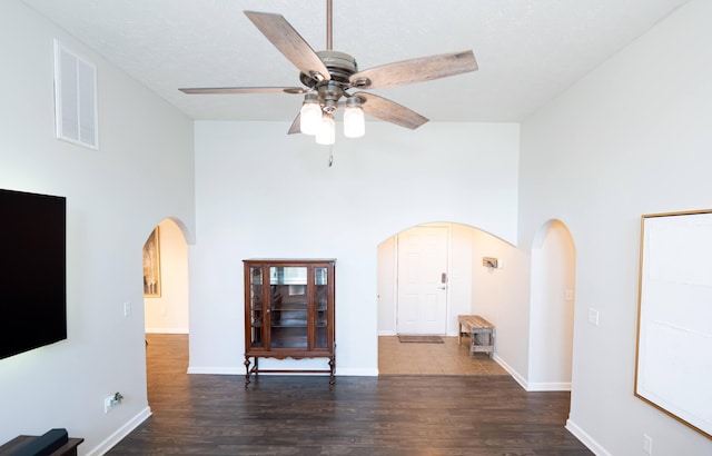 unfurnished living room with a towering ceiling, arched walkways, wood finished floors, and a ceiling fan