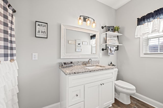 bathroom featuring baseboards, toilet, wood finished floors, and vanity