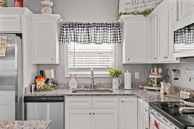 kitchen featuring white cabinets, light stone countertops, stainless steel appliances, and a sink