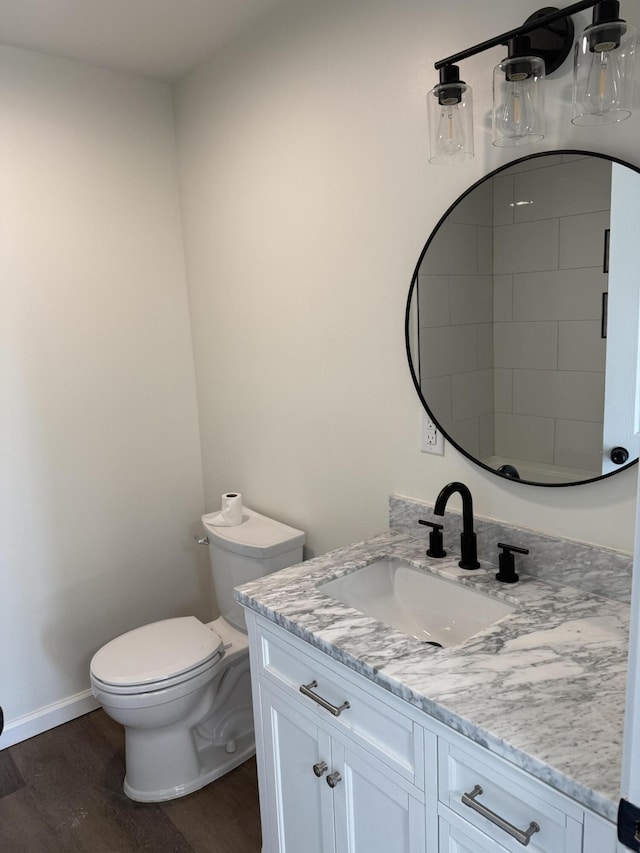 bathroom featuring baseboards, toilet, wood finished floors, and vanity