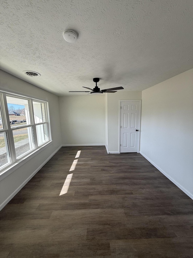 unfurnished room with visible vents, a ceiling fan, a textured ceiling, dark wood-style floors, and baseboards