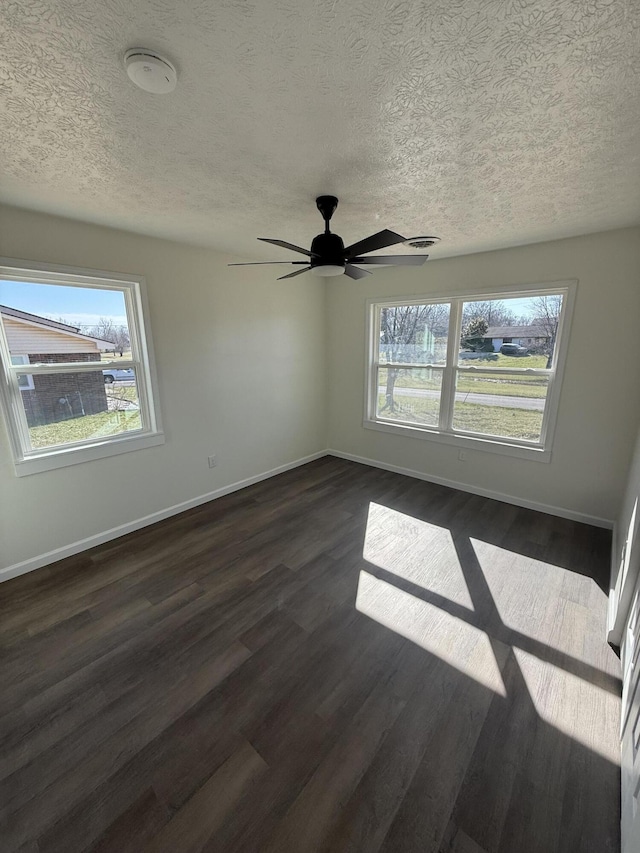 empty room featuring a textured ceiling, dark wood-type flooring, and baseboards