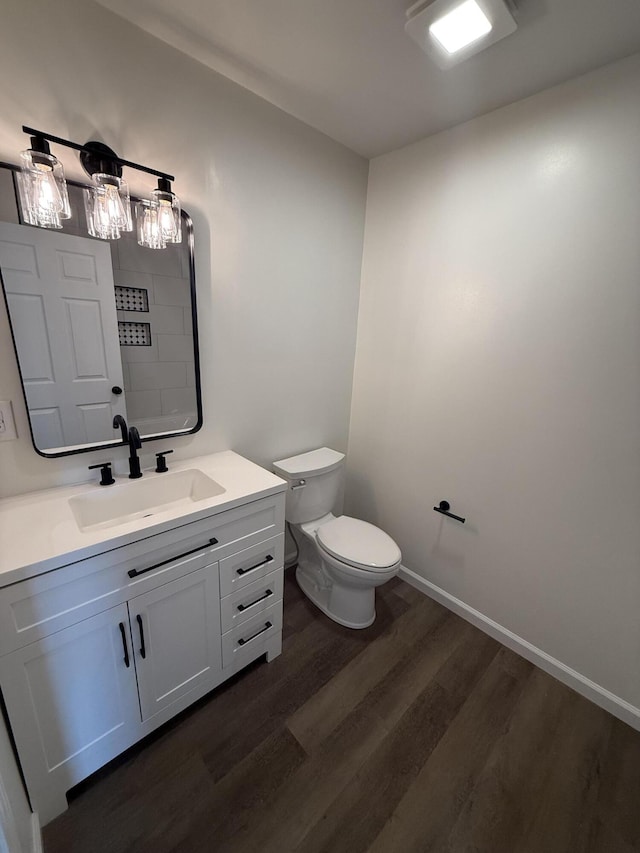 bathroom featuring baseboards, toilet, wood finished floors, and vanity