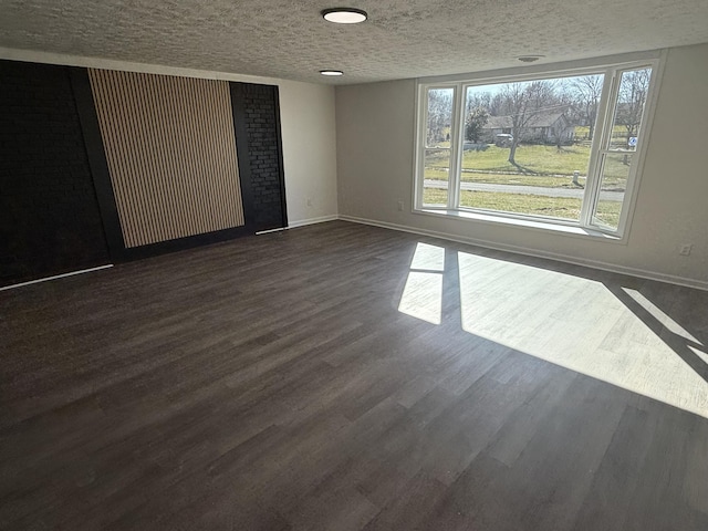 spare room featuring a textured ceiling, dark wood-type flooring, and baseboards