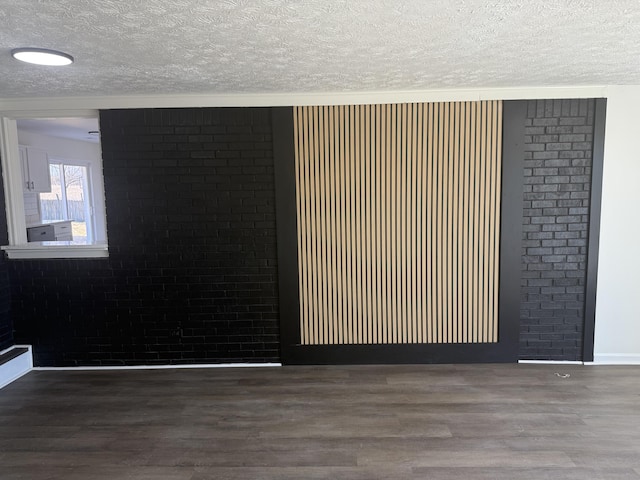 interior space featuring wood finished floors, brick wall, and a textured ceiling