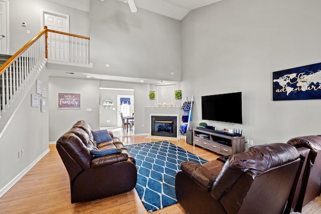 living area featuring baseboards, a fireplace with flush hearth, stairs, a high ceiling, and wood finished floors