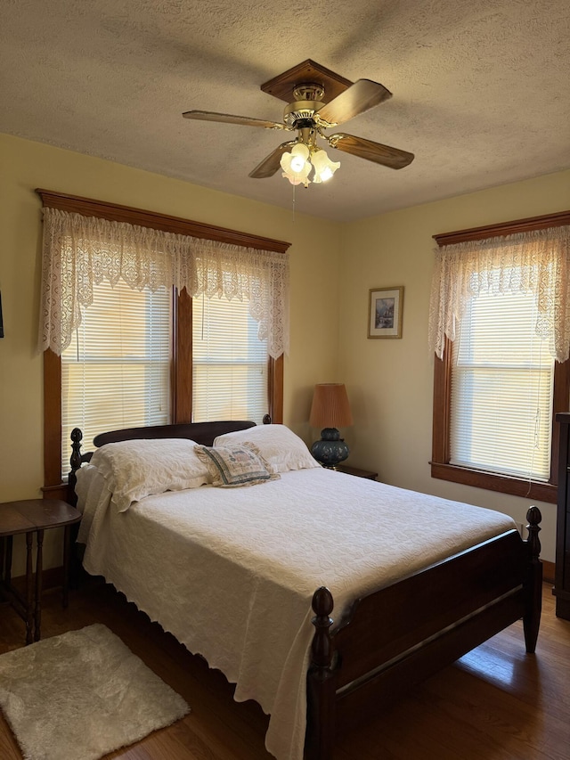 bedroom with multiple windows, a textured ceiling, ceiling fan, and wood finished floors