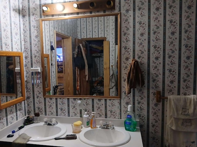 bathroom with a sink, double vanity, and wallpapered walls