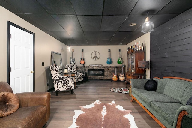 living room featuring a stone fireplace, wooden walls, wood finished floors, and a paneled ceiling