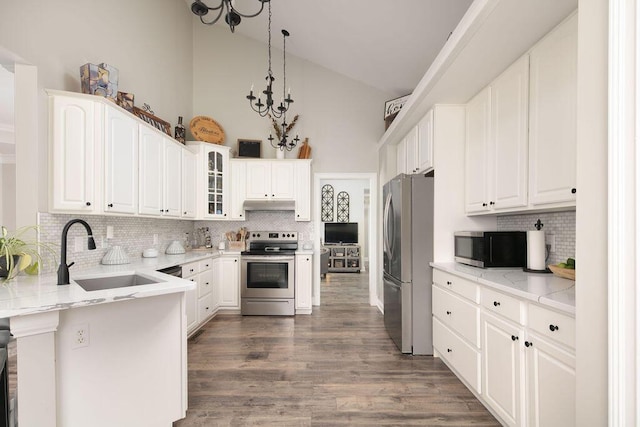 kitchen with a sink, stainless steel appliances, a peninsula, glass insert cabinets, and a chandelier