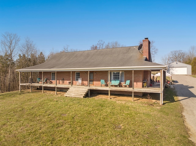 back of property featuring brick siding, a detached garage, a lawn, a chimney, and an outbuilding