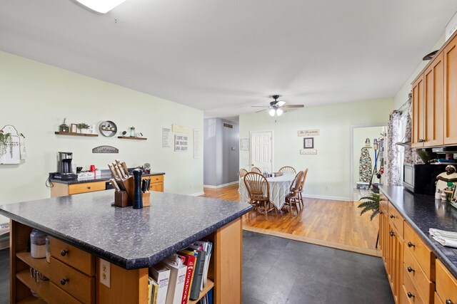 kitchen with open shelves, dark countertops, a center island, baseboards, and ceiling fan