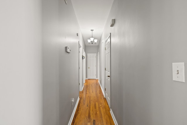 corridor with a notable chandelier, wood finished floors, and baseboards