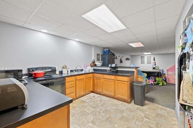 kitchen featuring a peninsula, a sink, black appliances, a paneled ceiling, and dark countertops