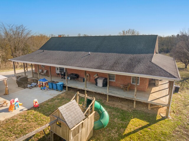 back of property featuring a deck, a playground, brick siding, and a shingled roof