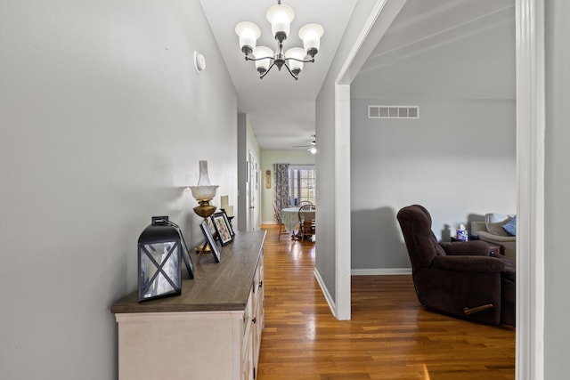 corridor featuring an inviting chandelier, wood finished floors, visible vents, and baseboards