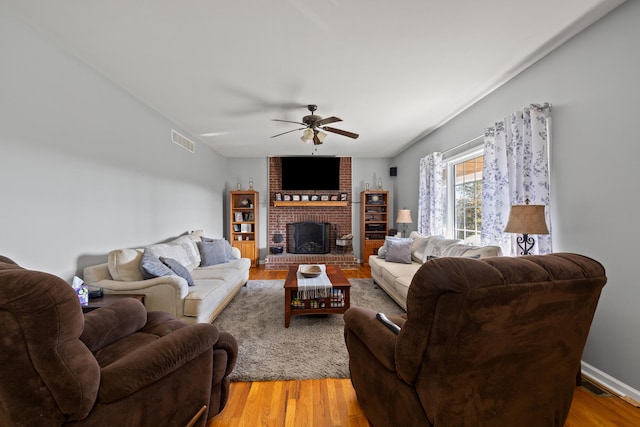 living area featuring visible vents, a brick fireplace, ceiling fan, and light wood finished floors