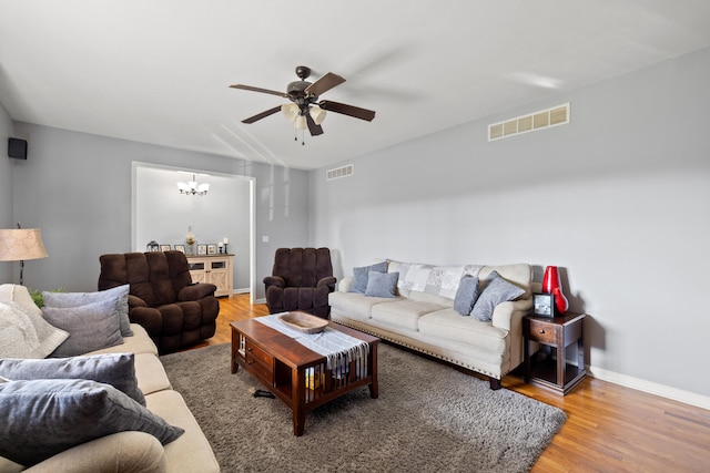 living area featuring visible vents, ceiling fan with notable chandelier, baseboards, and wood finished floors