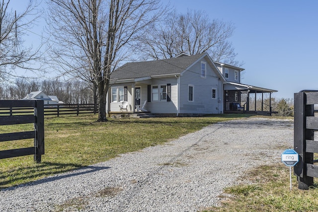 view of front of house with gravel driveway, a front lawn, and fence