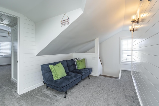 living area featuring wooden walls, baseboards, lofted ceiling, and carpet