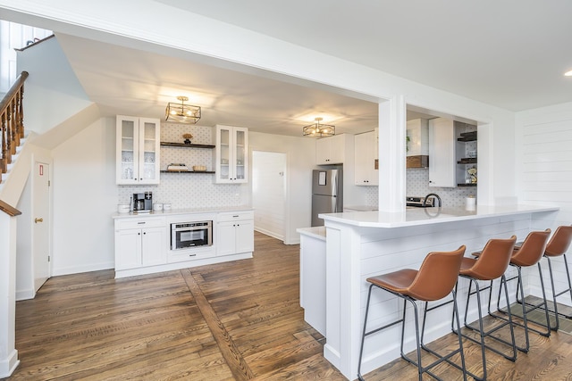 kitchen featuring a kitchen bar, open shelves, dark wood-style floors, stainless steel appliances, and glass insert cabinets