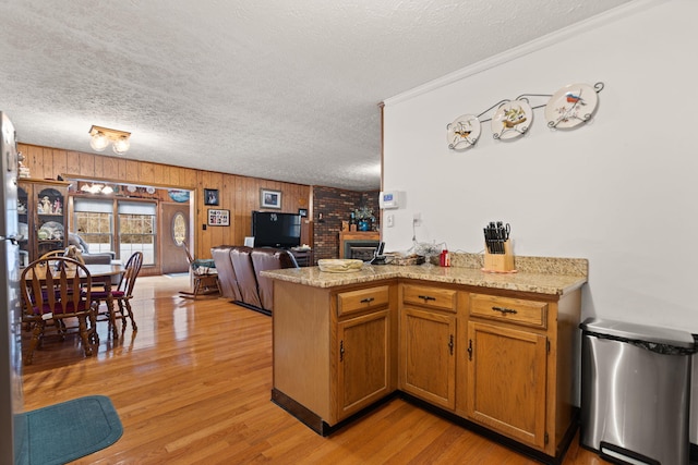 kitchen featuring a textured ceiling, open floor plan, a peninsula, brown cabinetry, and light wood finished floors