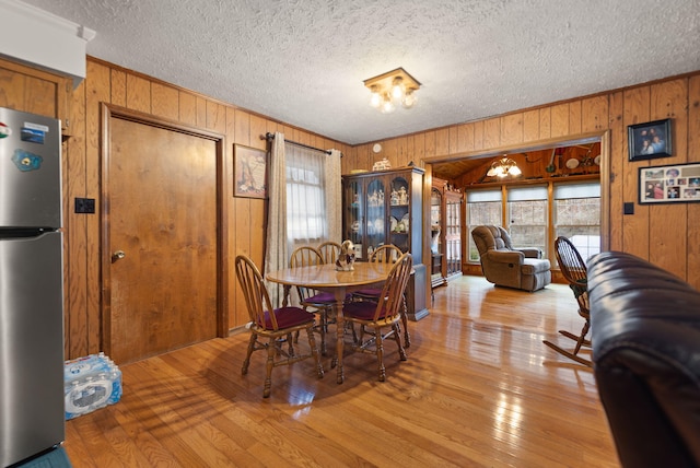 dining room featuring hardwood / wood-style flooring, wooden walls, and a textured ceiling