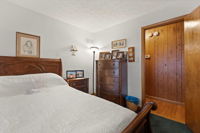 bedroom with visible vents, baseboards, a textured ceiling, and wood finished floors