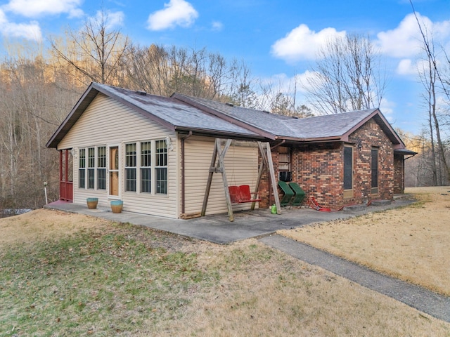 view of side of property with a yard, brick siding, a shingled roof, and a patio area