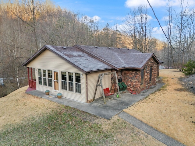 rear view of house featuring a lawn, a patio area, brick siding, and a shingled roof