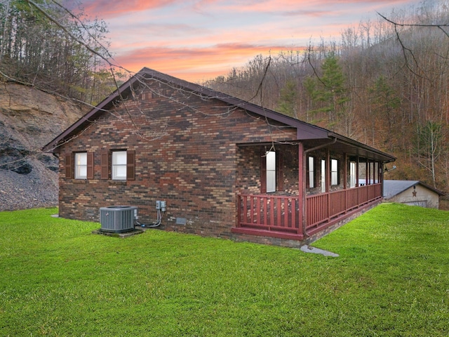 property exterior at dusk with cooling unit, a lawn, brick siding, and crawl space