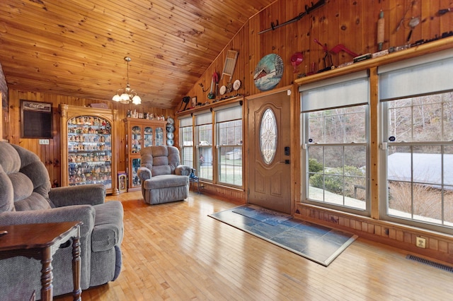 living area with a notable chandelier, visible vents, wooden walls, and wood-type flooring