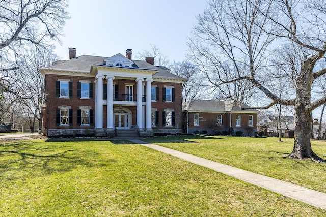 greek revival house with a front yard, a balcony, a chimney, french doors, and brick siding